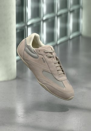 Lichtroze sneaker van suède en mesh met veter, ronde neus en beige accenten; afgebeeld tegen een minimalistische achtergrond.
