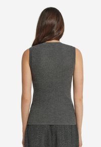 Kvinna med långt brunt hår som bär enärmlös grå ribbad topp, vänd bort, tillsammans med texturerade grå byxor.