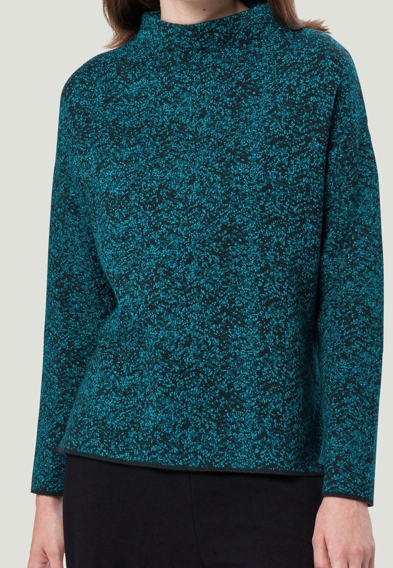 Haut à manches longues en teal et noir à motifs, avec un col montant, fabriqué en tissu texturé. Coupe décontractée, sans fermetures ni accents visibles.