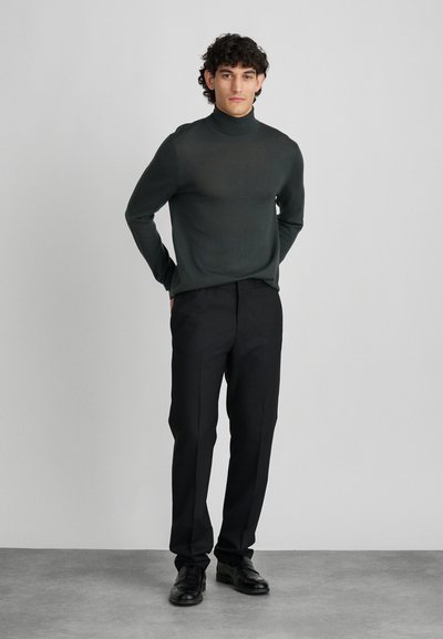 Temno zelena turtleneck pulover, slim fit, mehak na otip. V kompletu s črnimi krojenimi hlačami in črnimi usnjenimi čevlji. Preprost in sodoben dizajn.