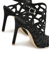 Schwarze High-Heel-Sandalen mit ausgeschnittenem Design, aus synthetischem Material, Knöchelriemen mit silberner Schnalle und beiger Sohle.