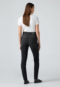 Musta farkkutyyppiset kapeat farkut, joissa on kapea istuvuus, korkea vyötärö, takataskut ja näkyvissä oleva merkkilappu takavyötäröllä.