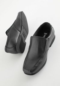 Chaussures noires en cuir à enfiler avec une finition lisse, bout rond et coutures contrastées. Semelles en caoutchouc offrant adhérence et stabilité.