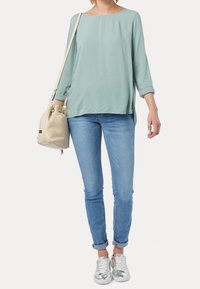 Ljusgrön oversized blus med trekvartslånga ärmar, kombinerad med ljusblå skinny jeans och silversneakers. Bär en beige axelväska.