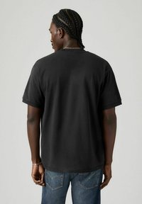 T-shirt en coton noir avec une coupe décontractée, des manches courtes et un col rond, vu de dos. Porté avec un jean bleu.