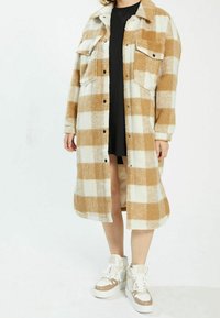 Rutig lång skjortjacka i tan och vitt med två bröstfickor, krage och knappar, tillverkad av ett mjukt, strukturerat tyg.