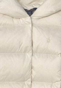 Bílá péřová bunda s kapucí, s prošívanými částmi. Obsahuje vyšívané logo na levé hrudi a hladkou nylonovou texturu.