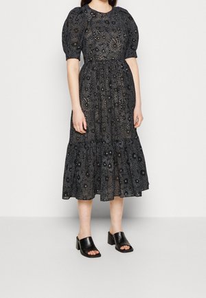 Woman wearing a black midi dress with puff sleeves and floral pattern, paired with black open-toe block heel mules.