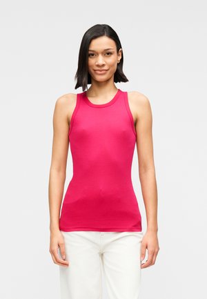 Débardeur ajusté en coton rose vif avec une texture lisse, design sans manches et col rond, porté avec un pantalon blanc.