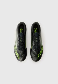 Chaussures de foot noires avec des accents vert fluo, design épuré, tige texturée et fermeture à lacets. Marquage F50 notable sur chaque chaussure.