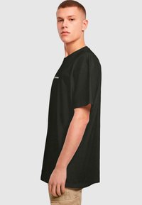 Černé bavlněné tričko s krátkými rukávy, kulatým výstřihem a bočním pohledem. Na přední straně je bílé textové nápis. Jednoduchý, uvolněný střih.