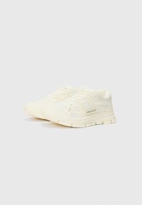 White athletic sneakers with a mesh and synthetic upper, textured sole, reinforced toe, and side accents. Features lace-up design.