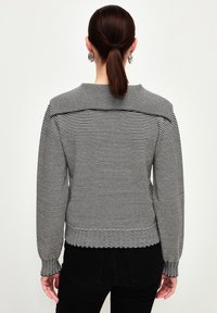 Pull rayé noir et blanc, design ajusté avec des manches longues et des poignets côtelés, présentant un col large et un tissu texturé.