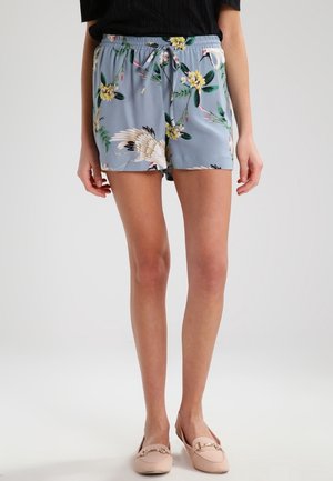 Lyseblå blomstrede shorts til kvinder med trækronemønster, snøre i taljen, båret med sort top og lyserøde loafers.
