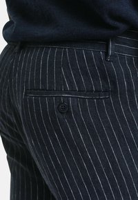 Navyblauwe broek met streepjes gemaakt van textuurstof, met een achterzak met een enkele knoopsluiting.