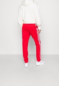 Červené tepláky z měkké látky s bílými bočními pruhy a volným střihem. Nošené s krémovou mikinou s kapucí a bílými teniskami.