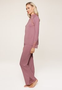 Ružičasti lounge komplet od meke tkanine, s dugim rukavima i čipkastim ukrasima na rukavima i rubovima hlača. Glatka, udobna prilagodba.