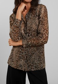 Blusa con stampa leopardata realizzata in tessuto trasparente, con un design a bottoni, maniche lunghe e una vestibilità rilassata con orlo curvo.