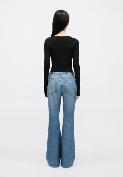 Top preto de mangas compridas combinado com jeans azuis flare de cintura subida. Características notáveis incluem uma textura canelada e desbotamento na bainha.