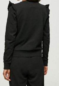 Sudadera negra con detalles de volantes en los hombros y patrones florales bordados en las mangas. Tejido suave, diseño ajustado y dobladillo acanalado.