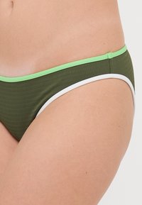 Olivgrüner Bikini-Unterteil mit strukturiertem Finish, versehen mit kontrastierenden hellgrünen und weißen elastischen Bändern entlang der Taille und Beinöffnungen.