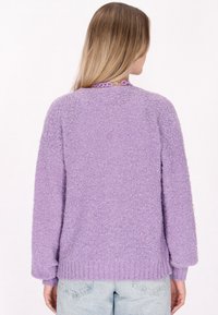 Lila bolyhos pulóver kerek nyakkivágással, hosszú ujjak, bordás szegéllyel és oversized fazonnal. Puha, texturált anyagból készült.