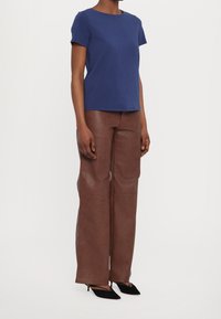 Camisa azul de manga corta combinada con pantalones acampanados de imitación cuero marrón y tacones negros de punta. Textura suave, diseño sencillo.
