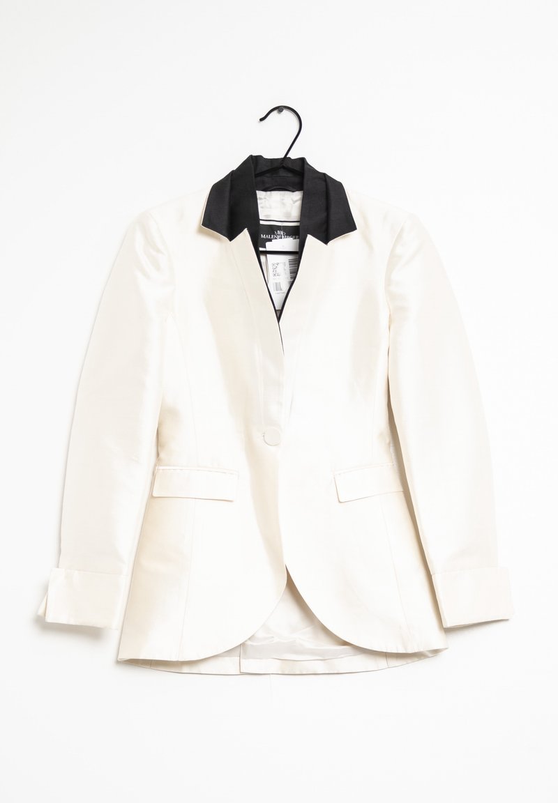 Bílý saténový blazer s černým límcem, jednořadým zapínáním, dvěma předními kapsami a dlouhými rukávy visící na černém ramínku na bílém pozadí.