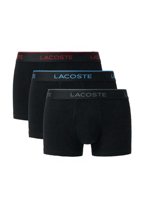 Tres calzoncillos bóxer negros de Lacoste apilados, cada uno con un logo en la cintura de diferente color: rojo, azul y gris.