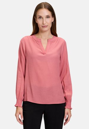 Chemisier rose à manches longues en tissu léger, avec un col en V et des poignets rabattus, offrant une coupe décontractée et une texture subtile.
