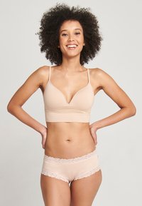 Sujeta pecho nudista con un diseño de escote en V y tirantes finos, combinada con boyshorts a juego con bordes de encaje, ambos en una suave tela elástica.