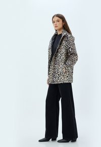 Oversized jakke i leopardprint lavet af stof, med to sidelommer, kante lapeller og en afslappet pasform. Båret med sorte vide bukser.