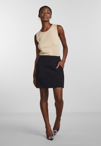 Haut sans manches beige associé à une mini-jupe noire. Comprend des poches latérales et est associé à des chaussures violettes avec un accent décoratif.