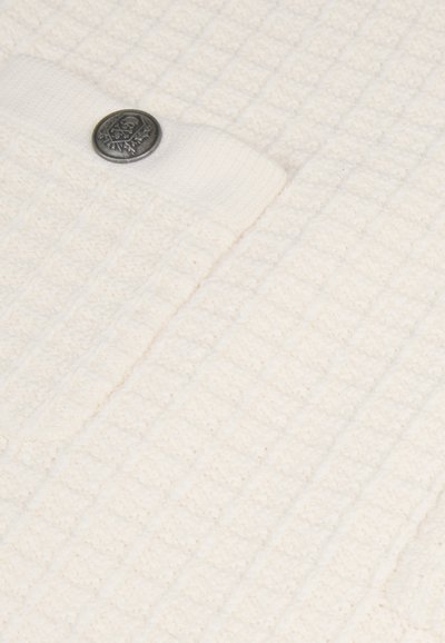 Tissu texturé couleur crème avec un motif côtelé, comportant un bouton en argent avec un design de crâne près du haut.