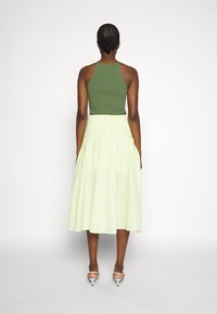 Débardeur vert à côtes associé à une jupe A-line jaune clair. La jupe présente une taille smockée et tombe sous les genoux.