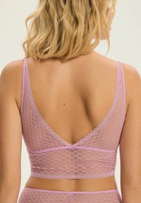 Różowy koronkowy biustonosz typu braletka z tyłem w kształcie litery V, z falbaniastymi krawędziami i teksturowanym wzorem. Materiał jest lekki i półprzezroczysty.