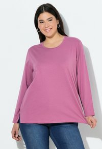 T-shirt a maniche lunghe, con scollo rotondo, di colore lilla chiaro, realizzato in tessuto morbido con vestibilità rilassata e spacchi laterali per comfort e libertà di movimento.