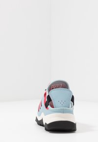 Kengät, joissa on vaaleansininen yläosa, punaiset raidat ja mustat yksityiskohdat. Varustettu pyöristetyllä kantapäällä, tekstuuripohjalla ja pehmustetulla sisätilalla mukavuutta varten.