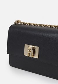 Borsa a mano nera in pelle con finitura testurizzata, chiusura in metallo dorato e tracolla a catena. Forma compatta e rettangolare con parte superiore liscia.