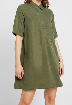 Kaki groene overhemdjurk met een kraag, korte opgerolde mouwen, een borstzak en een ontspannen pasvorm. Gladde textuur en minimalistisch ontwerp.