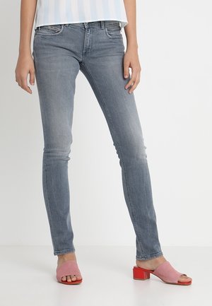 Jeans ajustados de color azul con un acabado desgastado, combinando algodón con un ligero estiramiento. Combinados con unas mules rosas de punta abierta que cuentan con un tacón bloque rojo.