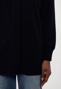 Mørkeblå langermet topp med sammenpressede mansjetter, myk tekstur og rett snitt, kombinert med lyseblå denimjeans.