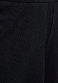 Svart ribbad tyg med en slät textur, som visar vertikala linjer och en figurnära design, med en sömlös midja och ingen synlig hårdvara.