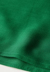 Tissu vert avec une texture lisse, présentant un léger éclat. Il présente un motif tissé serré et des bords cousus, mettant en avant sa durabilité.