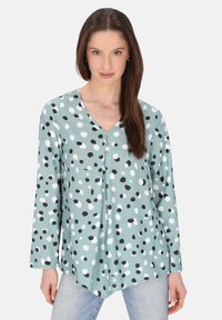 Langarmshirt van mintgroene stof, met een V-hals, zwart-witte stippen en drie decoratieve knopen aan de voorkant.