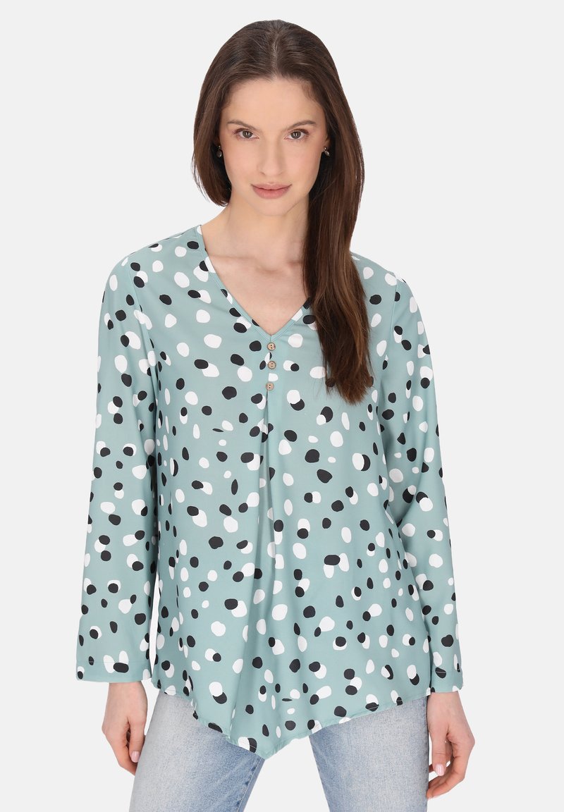 Langarmshirt van mintgroene stof, met een V-hals, zwart-witte stippen en drie decoratieve knopen aan de voorkant.