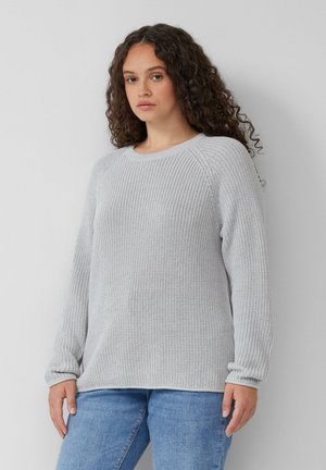 Pull en tricot gris clair avec une texture côtelée, un col rond et des manches longues. Associé à un jean bleu, mettant en avant une coupe décontractée.