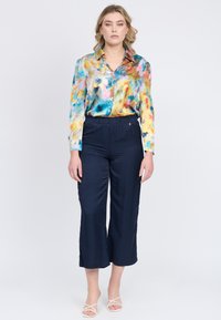 Blusa di satin multicolore con motivi astratti simili a pittura, abbinata a culotte blu navy con vita elastica e sandali bianchi con cinturini.