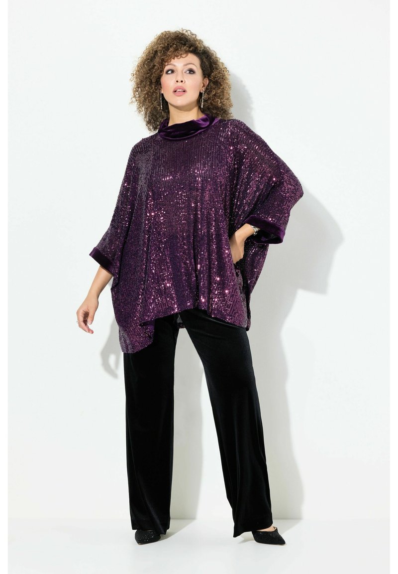 Poncho viola con paillettes e collo alto, abbinato a pantaloni larghi in velluto nero. Presenta maniche ampie e una texture morbida per il massimo del comfort.
