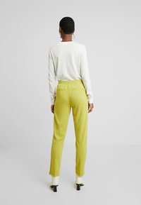 Yellow, tailored pants with a smooth texture, side pockets, and a relaxed fit, paired with a light gray long-sleeve shirt.